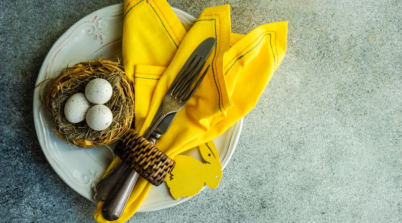 Top view of Easter table setting on concrete table with nest and yellow napkin