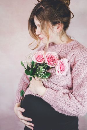 Portrait of pregnant woman in pink knit sweater holding pink rose bouquet