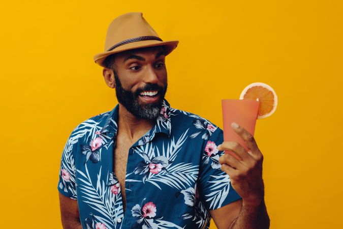 Male looking happy at his cocktail while wearing colorful shirt with yellow background