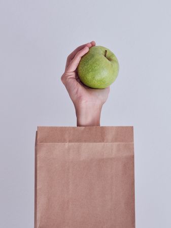 Crop person reached out from paper bag with green apple