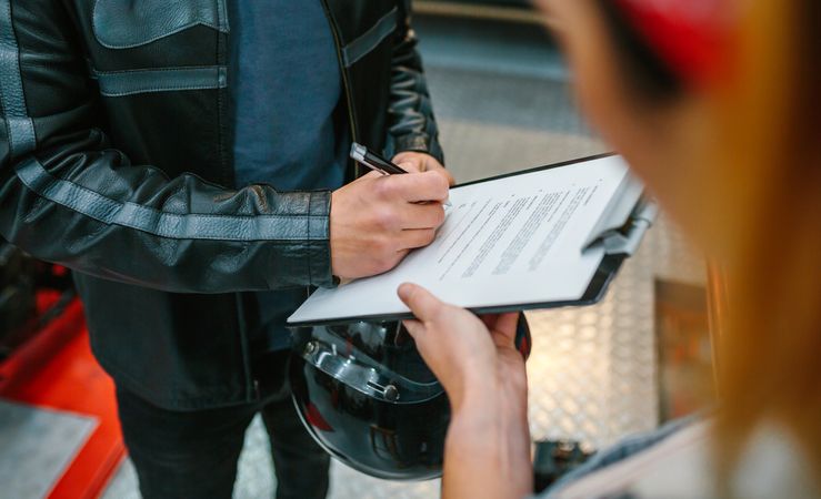 Biker man signing insurance policy on workshop while female mechanic holding clipboard