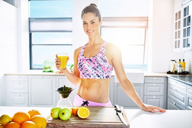 Muscular fit woman with fresh fruit juice in bright kitchen