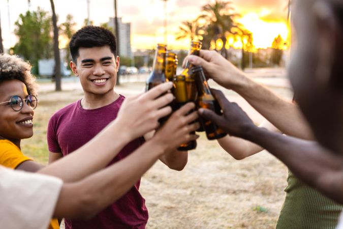 Happy multi-ethnic friends and clinking their beer bottles together outside