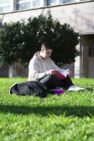 Young student sitting in park with his notes
