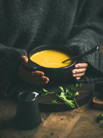 Blonde woman with warm yellow soup in dark bowl and cream