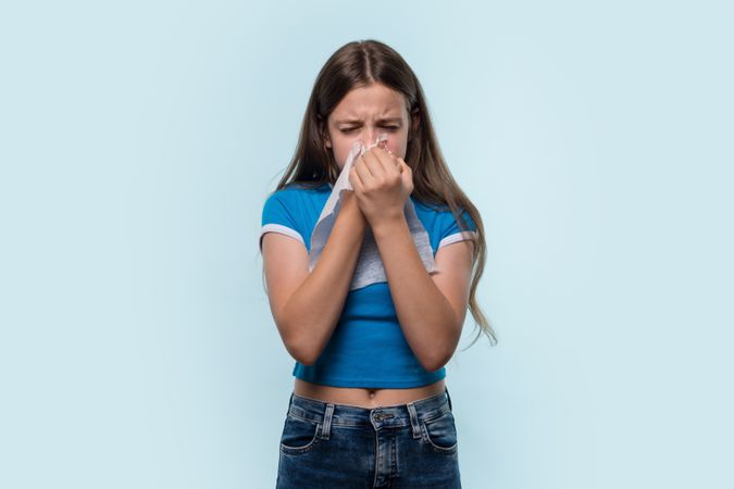 Girl sneezing into tissue, showing symptoms of cold or allergy