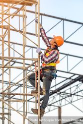 Man in orange bump cap climbing a scaffolding 0JJzr0
