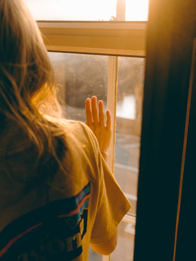 Woman in orange shirt looking outdoor through window during golden hours