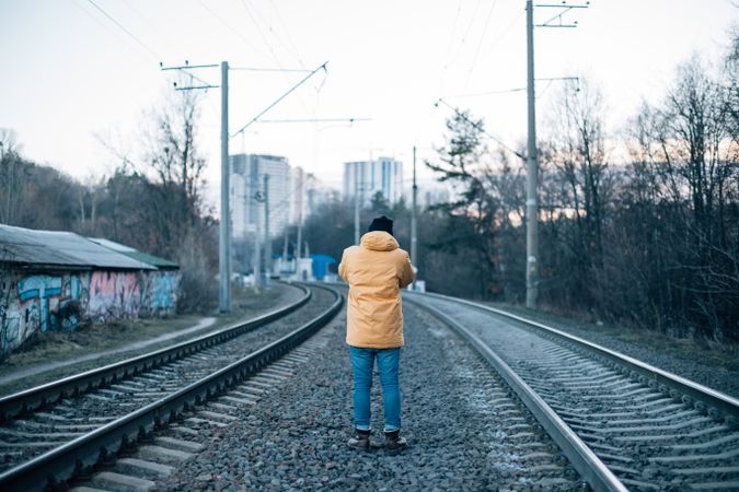 Man in yellow jacket in between train tracks