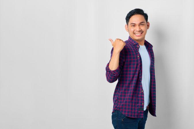 Smiling Asian male in grey studio with pointing thumb behind him