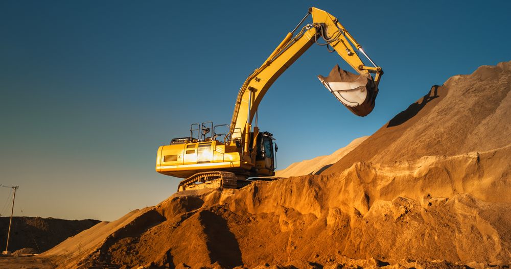 Construction Site On A Sunny Day: Industrial Excavator Digging Sand To Lay Foundation for Building New Apartment Complex. Workers Operating Heavy Machinery To Complete A Real Estate Project.