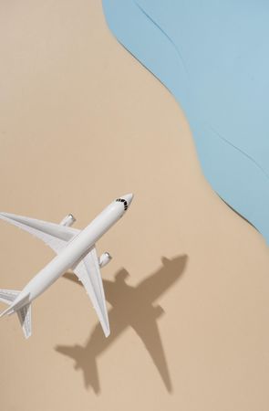 Top view of model airplane with shadow over beige and blue water beach scene