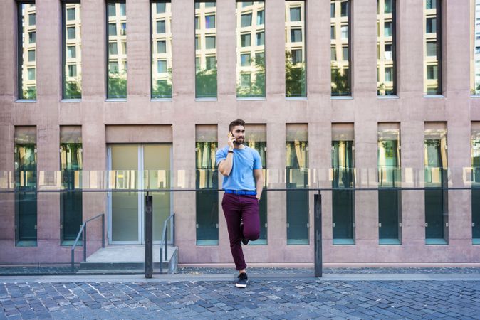 Bearded man leaning on glass railing outside building talking on mobile phone