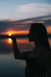 Content woman in swimwear holding sun on beach at sunset