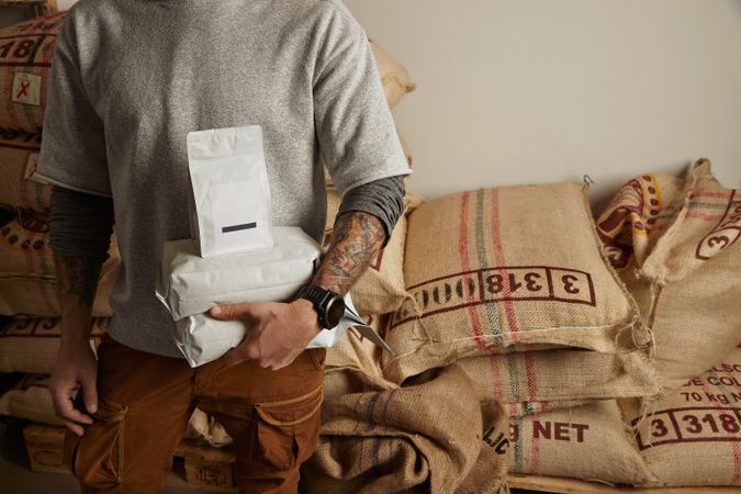 Tattooed barista holds blank package bags with freshly baked coffee beans