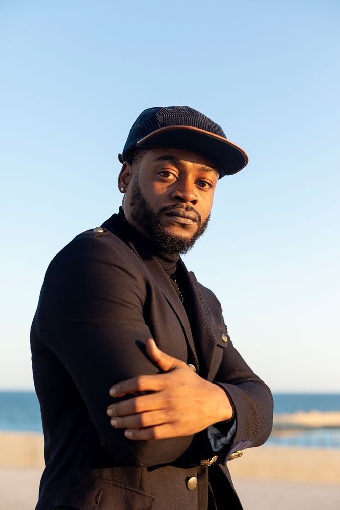 Front view of bearded man with cap arms crossed while looking at camera on sunny day