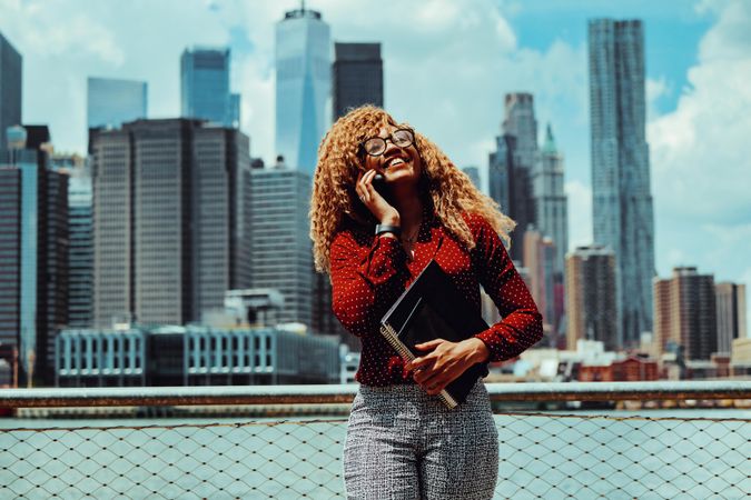 Smiling professional Black female speaking on phone with Manhattan in the background