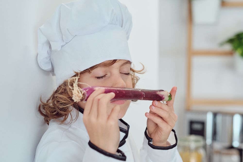 Preteen boy in chef cap and suit sniffing red leek