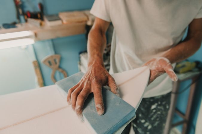 Man in respirator polishing surf board in workshop