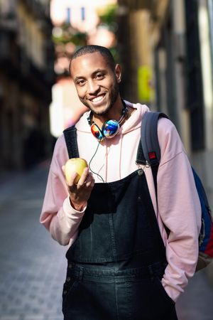 Vertical shot of smiling male on European street eating an apple