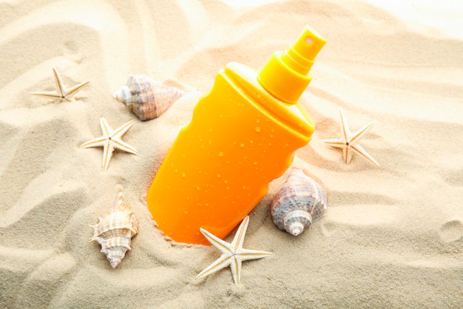 Sunscreen with starfish and seashells on clear sea sand, closeup and space for text. Summer vacation