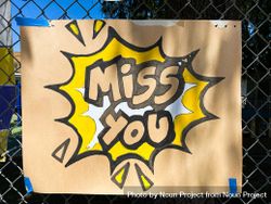 Close up shot of brown sign taped to school fence with the words “miss you” 5ngJ84