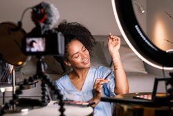 Woman with camera and light ring filming herself demoing different foundations