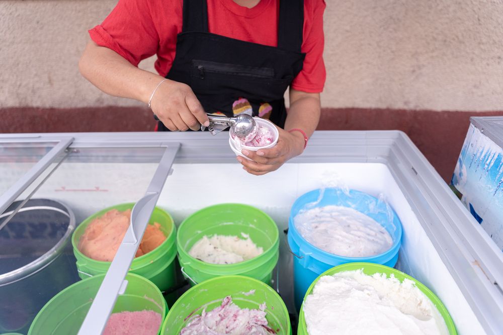 An Hispanic adult woman is serving blackberry and cheese ice cream on a cup in the street