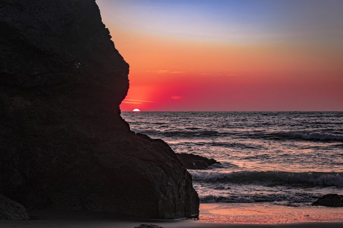 Colorful sunset seen from behind cliffs of rocky beach