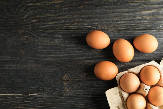 Brown chicken eggs in carton box on wooden table, space for text and top view