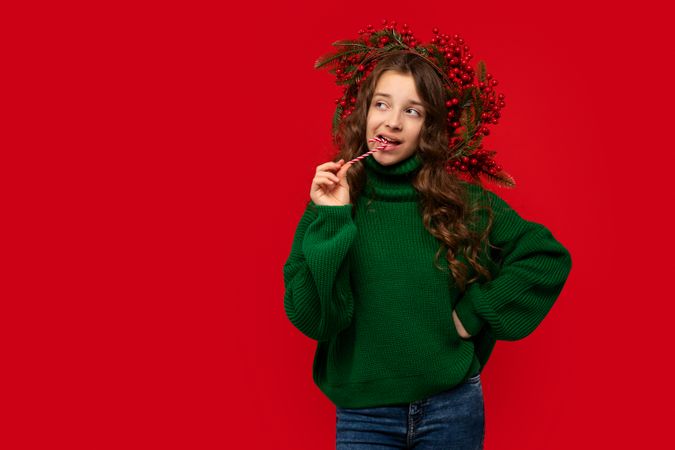 Young girl in green sweater biting a candy cane