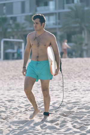 Male surfer walking on beach with board attached to his leg with leash