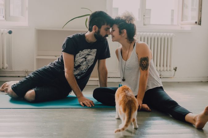 Loving couple cuddling on floor while cat walking around