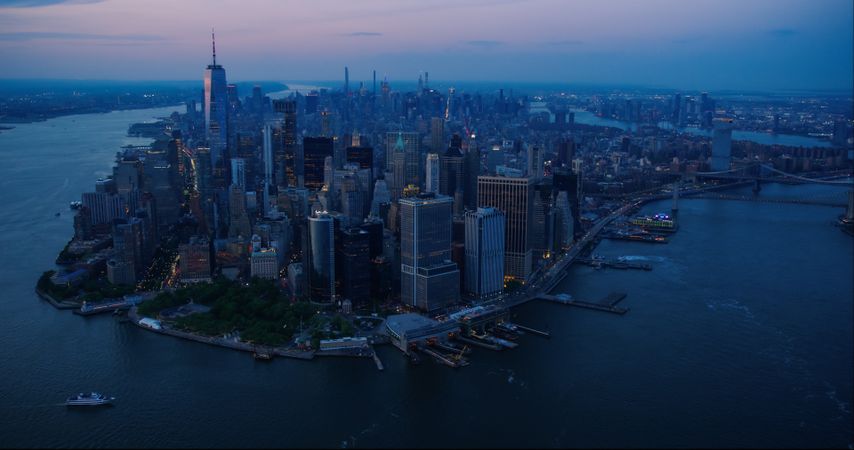 Evening Panorama Around the Wall Street Financial District in New York City, USA. Dark Aerial Shot with Lit Office Buildings and Skyscrapers on a Summer Night with Deep Blue Sky