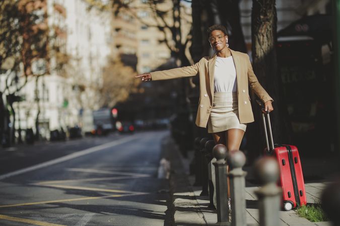 Stylish Black woman with luggage hitchhiking on street