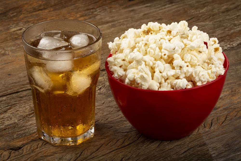 Bowl with salted popcorn and soda on the table.