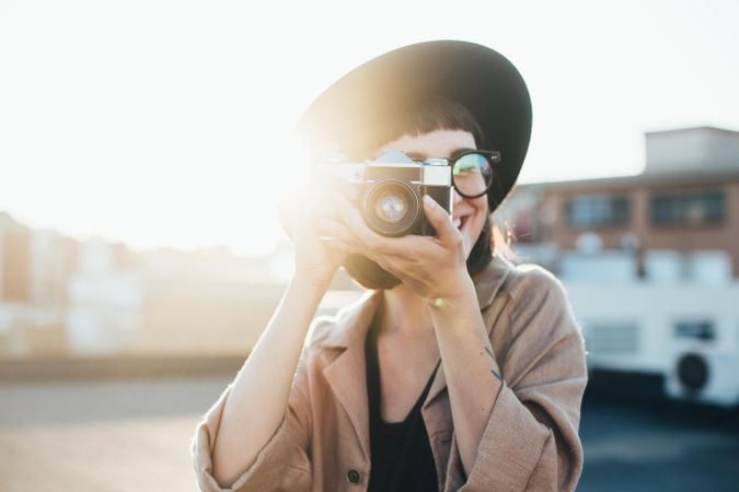 Backlit woman with camera taking picture outside at sunset