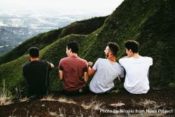 Back view of four young men sitting against mountainous landform 4OJmJ5
