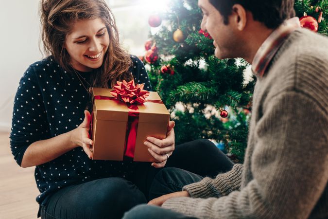 Smiling couple exchanging Christmas gifts in their living room