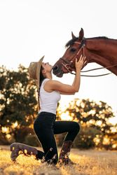 Young woman in hat walking with her horse in the countryside at sunset