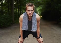 Athletic man with hands on knees in forest path and looking at camera