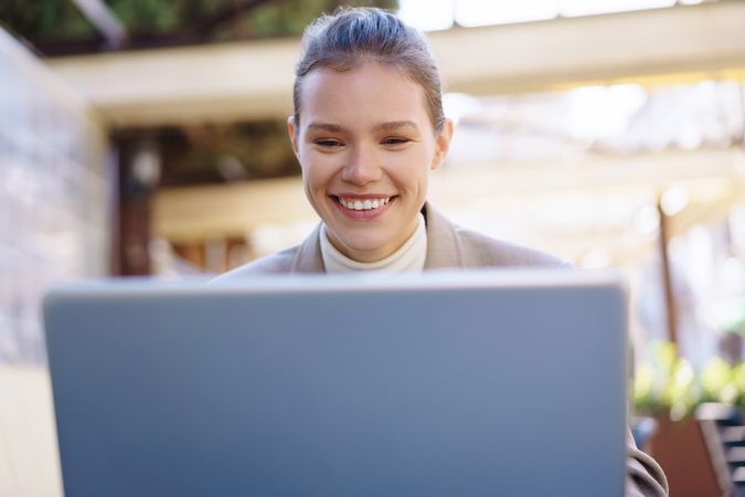 A smiling woman actively engaged in online work using a laptop in a modern workspace