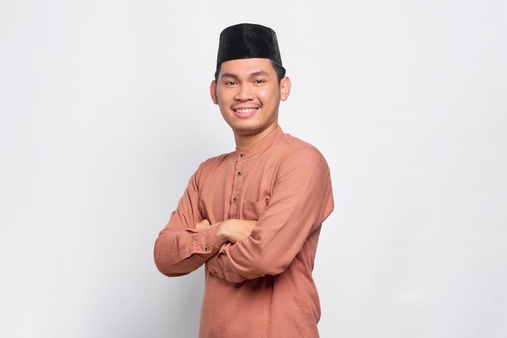 Portrait of Muslim man in kufi head wear smiling arms crossed