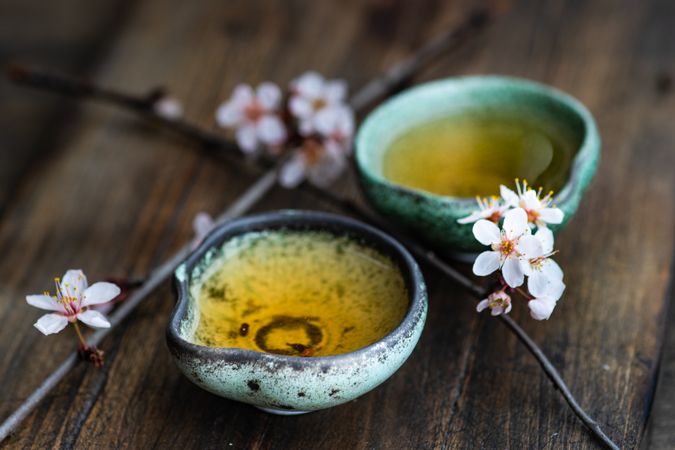Green tea in cups and blooming peach tree branch on wooden table