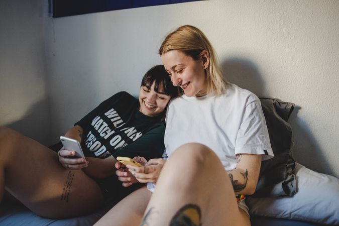 Happy lesbian couple using smartphone on bed