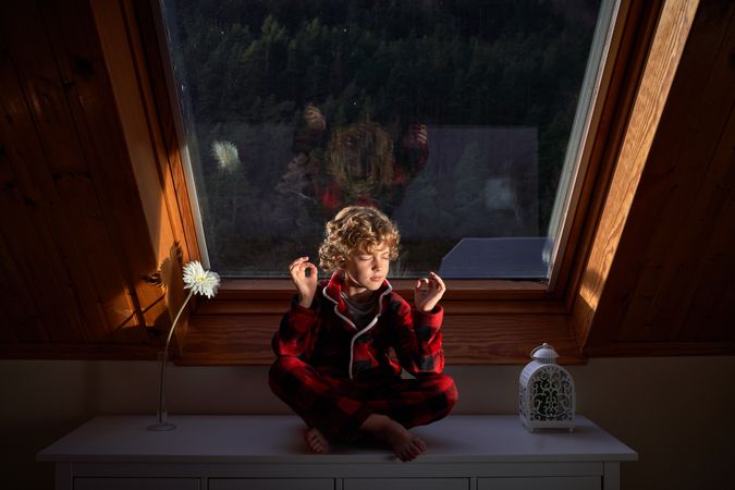 Adorable boy sitting in Lotus pose on chest of drawers
