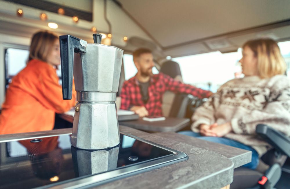 Italian stove top espresso in foreground of friends sitting in back of camper