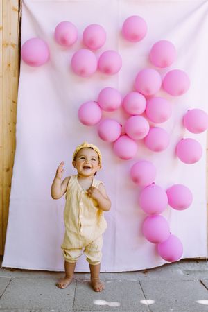 Delighted boy standing near wall with balloons
