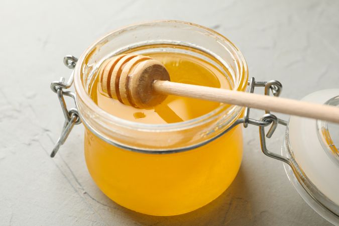 Glass jar with honey and dipper on neutral background, close up
