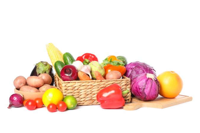 Wicker basket, wood board and vegetables isolated on blank background